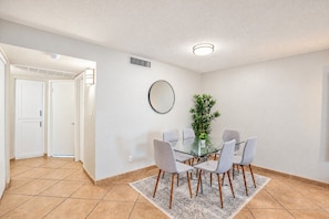 A modern dining area with a glass table surrounded by chairs, a potted plant, and a wall-mounted mirror.
