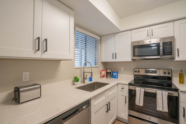 A modern kitchen with white cabinetry, a stainless steel microwave, a built-in oven, and a dishwasher.