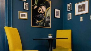 A room with dark blue walls, two yellow chairs, a small round table with a white vase, and several framed pictures on the wall. - The Great Gatsby - Luxury Historic Riverside (Jacksonville)