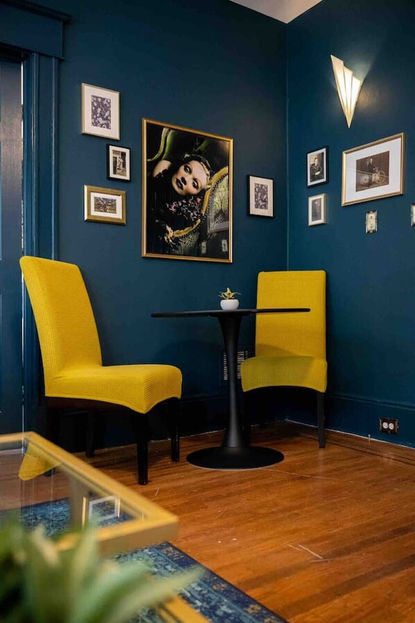 A room with dark blue walls, two yellow chairs, a small round table with a white vase, and several framed pictures on the wall.