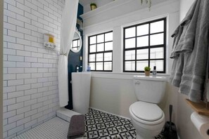 Un baño con inodoro blanco, zona de ducha y ventana con vistas.