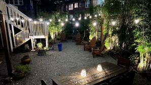 An outdoor patio area with a wooden table and chairs, surrounded by potted plants and string lights. - The Great Gatsby - Luxury Historic Riverside (Jacksonville)