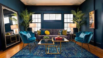 A modern living room with a dark blue sofa, two blue armchairs, a glass coffee table, and a patterned rug.