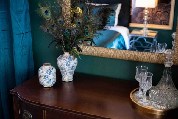 Un aparador de madera con jarrones decorativos y un espejo que refleja una habitación con cortinas color turquesa y un cuadro enmarcado.