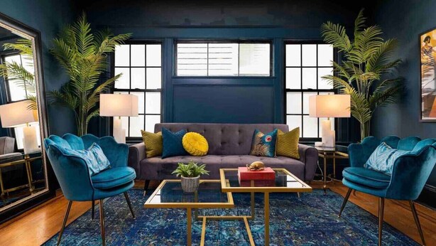 A modern living room with a dark blue sofa, two blue armchairs, a patterned rug, and a glass coffee table. - The Great Gatsby - Luxury Historic Riverside (Jacksonville)