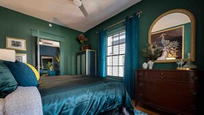 A bedroom with a large bed, a dresser, a mirror, and a window with curtains. - The Great Gatsby - Luxury Historic Riverside (Jacksonville)