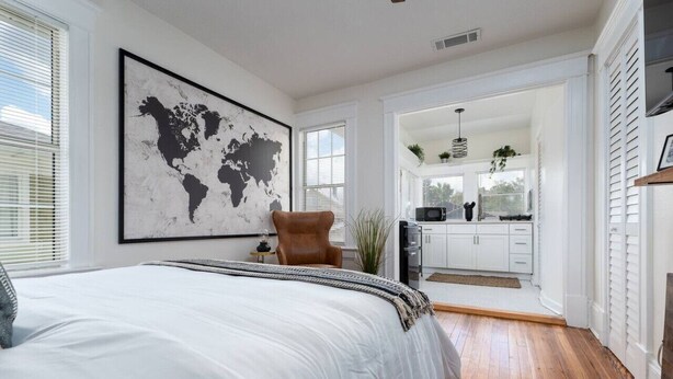 Een slaapkamer met een groot bed, een wereldkaart als kunstwerk, en uitzicht op een keuken.