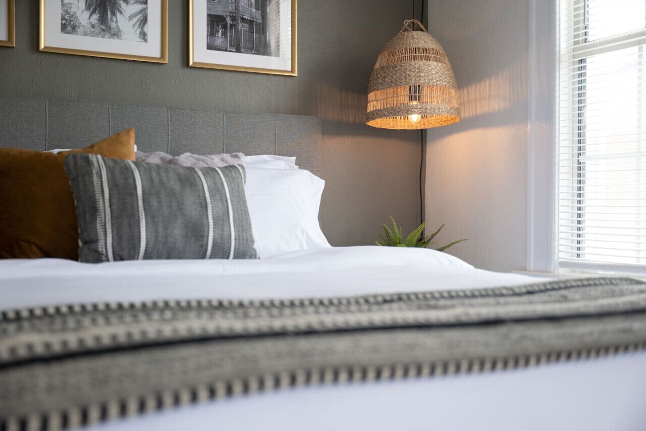 A neatly made bed with pillows and a blanket, a wall-mounted lamp, and framed pictures on the wall.