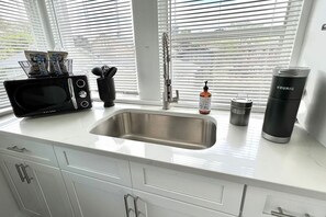 Een keuken met een roestvrijstalen spoelbak, een magnetron, een waterkoker en een koffiezetapparaat op het aanrecht.