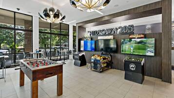 A modern indoor space with a foosball table, multiple screens, and a large TV displaying a golf game.