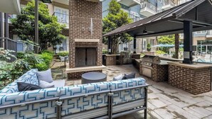 Eine Terrasse mit Kamin aus Ziegelsteinen, Sitzgelegenheiten und einem Grill.