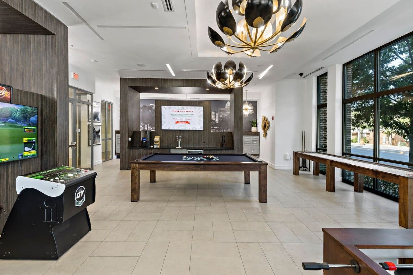Une table de billard dans un espace intérieur moderne, avec une table de pool, une table de baby-foot et une grande fenêtre offrant une vue sur l’extérieur.