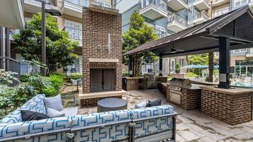 An outdoor patio with a brick fireplace, a barbecue grill, and a patterned sofa.