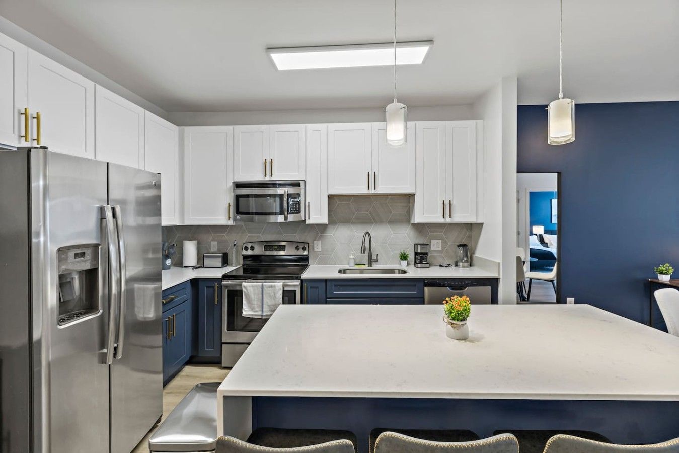 A modern kitchen with stainless steel appliances, a central island, and a view into a bedroom.