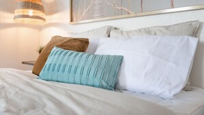 A neatly made bed with white and teal pillows, a hanging light fixture, and a framed artwork above. - Bright Airy Luxurious Abode in Walkable Riverside (Jacksonville)
