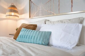A neatly made bed with white and teal pillows, a hanging light fixture, and a framed artwork above. - Bright Airy Luxurious Abode in Walkable Riverside (Jacksonville)