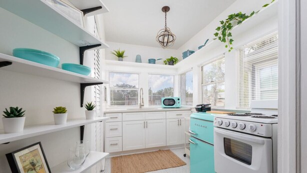 A kitchen with white cabinets, a teal stove, and a microwave. There are potted plants on the shelves and a hanging plant. - Bright Airy Luxurious Abode in Walkable Riverside (Jacksonville)
