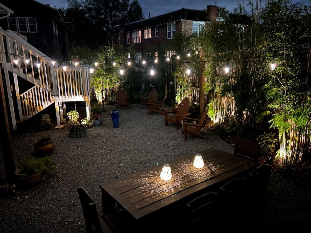 Un patio al aire libre con mesa de madera, sillas y luces colgantes.