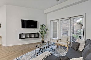 A modern living room with a flat-screen TV, a potted plant, a sofa, and a patterned rug. - Near CPCC & light Rail | Pool, Gym, W/D & Parking (Charlotte)