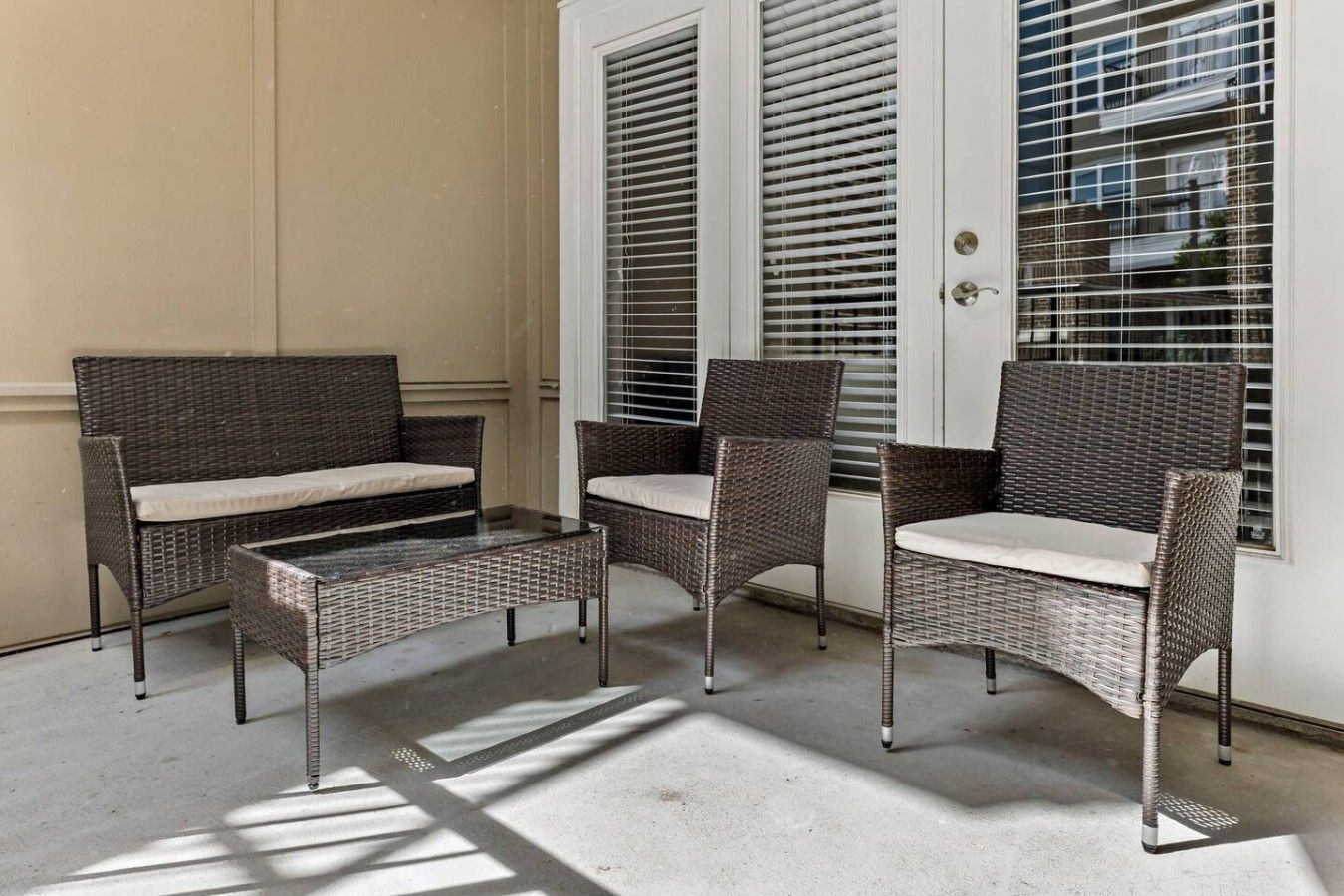 A patio area with wicker furniture, including a sofa and chairs, near a white door with blinds.