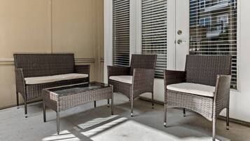 A patio area with wicker furniture, including a sofa and chairs, near a white door with blinds.