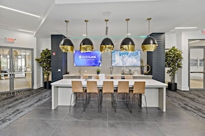 Une cuisine moderne dotée d’un îlot central, de tabourets de bar, de luminaires suspendus et d’un téléviseur à écran plat diffusant la chaîne d’information « NEWSLIVE ».