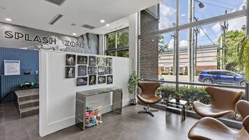 Interior de un salón de peluquería canina, con un letrero que dice 'Zona de Chapuzones', una pared con fotos de perros, un mostrador de recepción y un amplio ventanal con vistas a la calle.