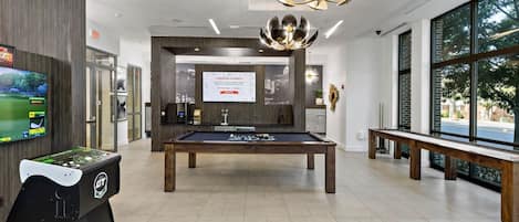 Mesa de billar en un entorno interior moderno con mesa de pool, mesa de fútbol de mesa y un ventanal con vistas al exterior.
