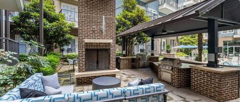 An outdoor patio area with a brick fireplace, a barbecue grill, and a seating area with patterned cushions.
