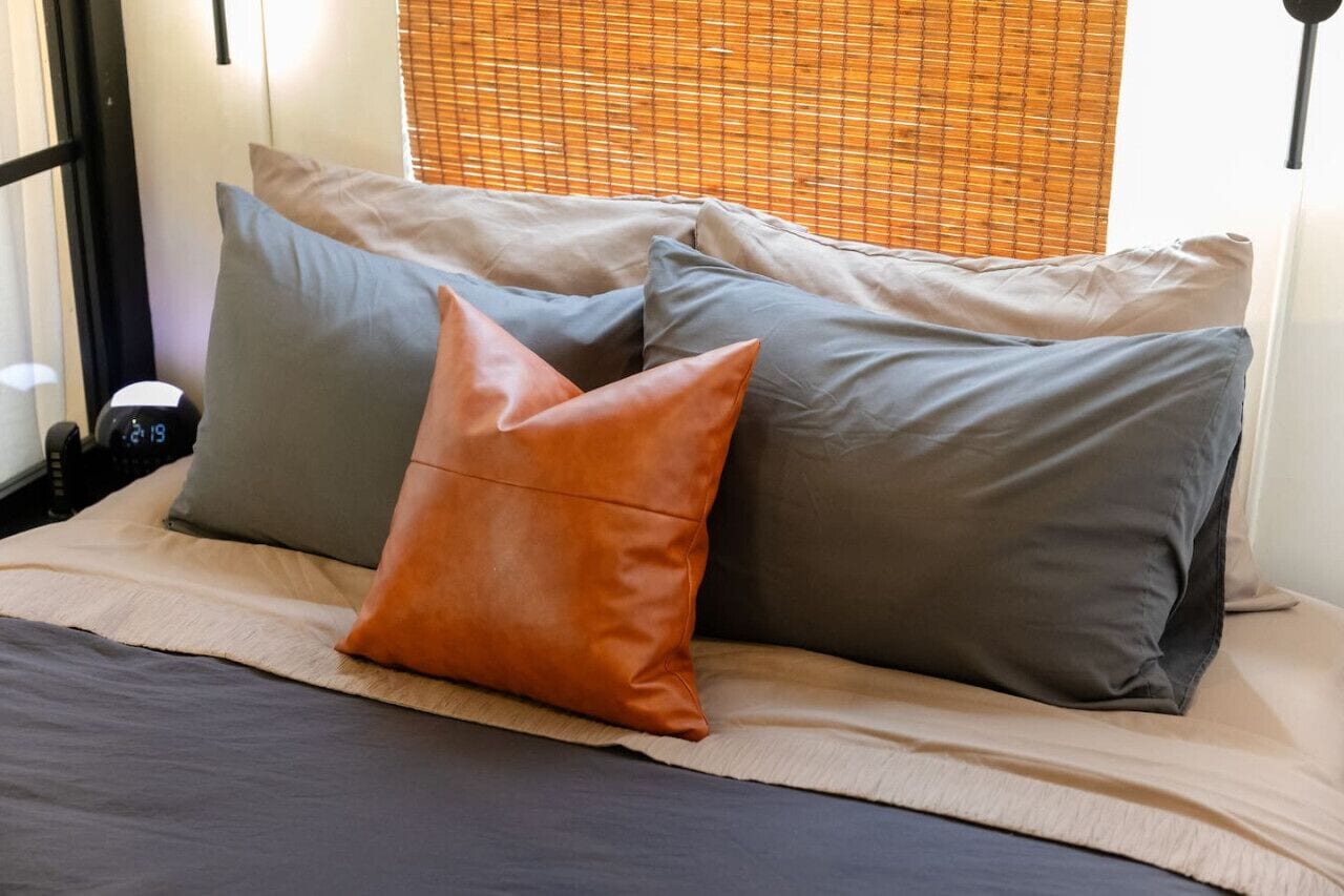 A bed with multiple pillows and a bedside table with a clock.