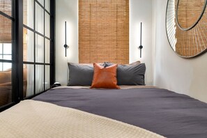 A modern bedroom with a large bed, a window with blinds, and a round mirror on the wall. - Wabi-Sabi Inspired Studio w Bikes, Walk to River (Jacksonville)