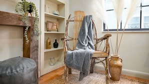 A rustic wooden chair with a grey throw blanket, a woven rug, and a vase with dried plants. - Wabi-Sabi Inspired Studio w Bikes, Walk to River (Jacksonville)