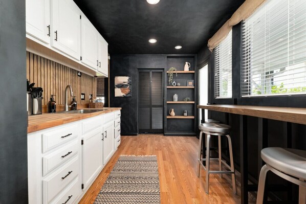 Una cocina moderna con armarios blancos, encimera de madera y techo negro.