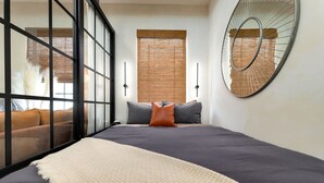 Un dormitorio con una cama grande, un sofá, un espejo y una ventana con persianas.