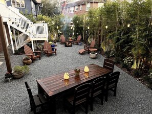 A wooden deck with a table and chairs, surrounded by potted plants and a fire pit.