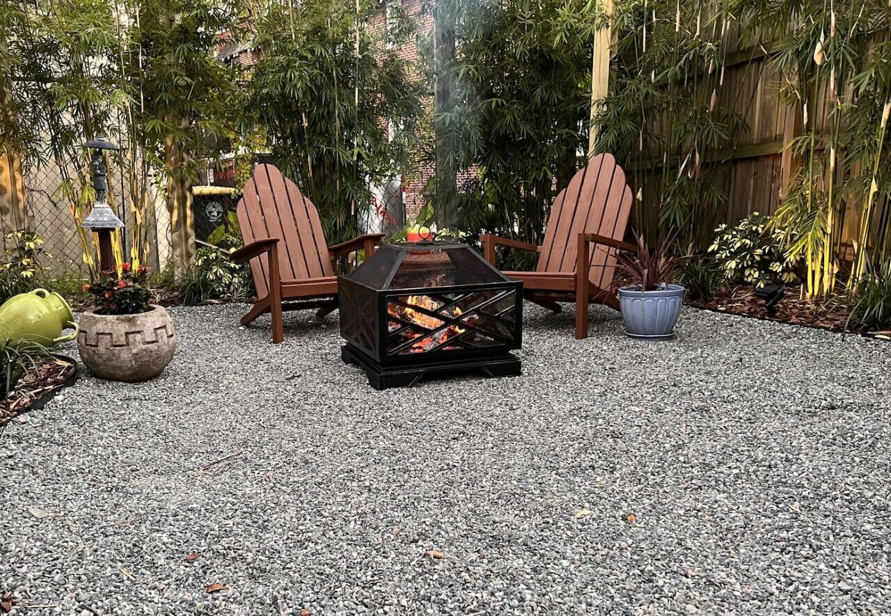 Um pátio com duas cadeiras Adirondack, uma lareira e um vaso de planta.