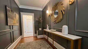 Un couloir orné d’un tapis à motifs, une console sur laquelle est posé un vase, un miroir et une porte donnant sur une autre pièce.