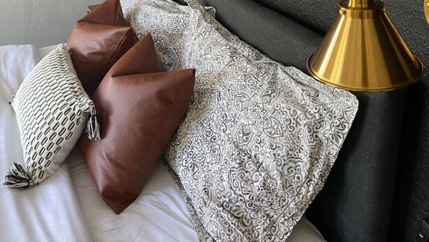 Une chambre à coucher comprenant un lit, des oreillers, un tableau abstrait encadré, une lampe fixée au mur et un mur à texture.