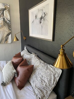 Une chambre à coucher comprenant un lit, des oreillers, un tableau abstrait encadré, une lampe fixée au mur et un mur à texture.