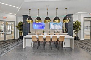 Un área de cocina moderna con una isla central, taburetes de bar, iluminación colgante y un televisor mostrando 'NEWSLIVE'.