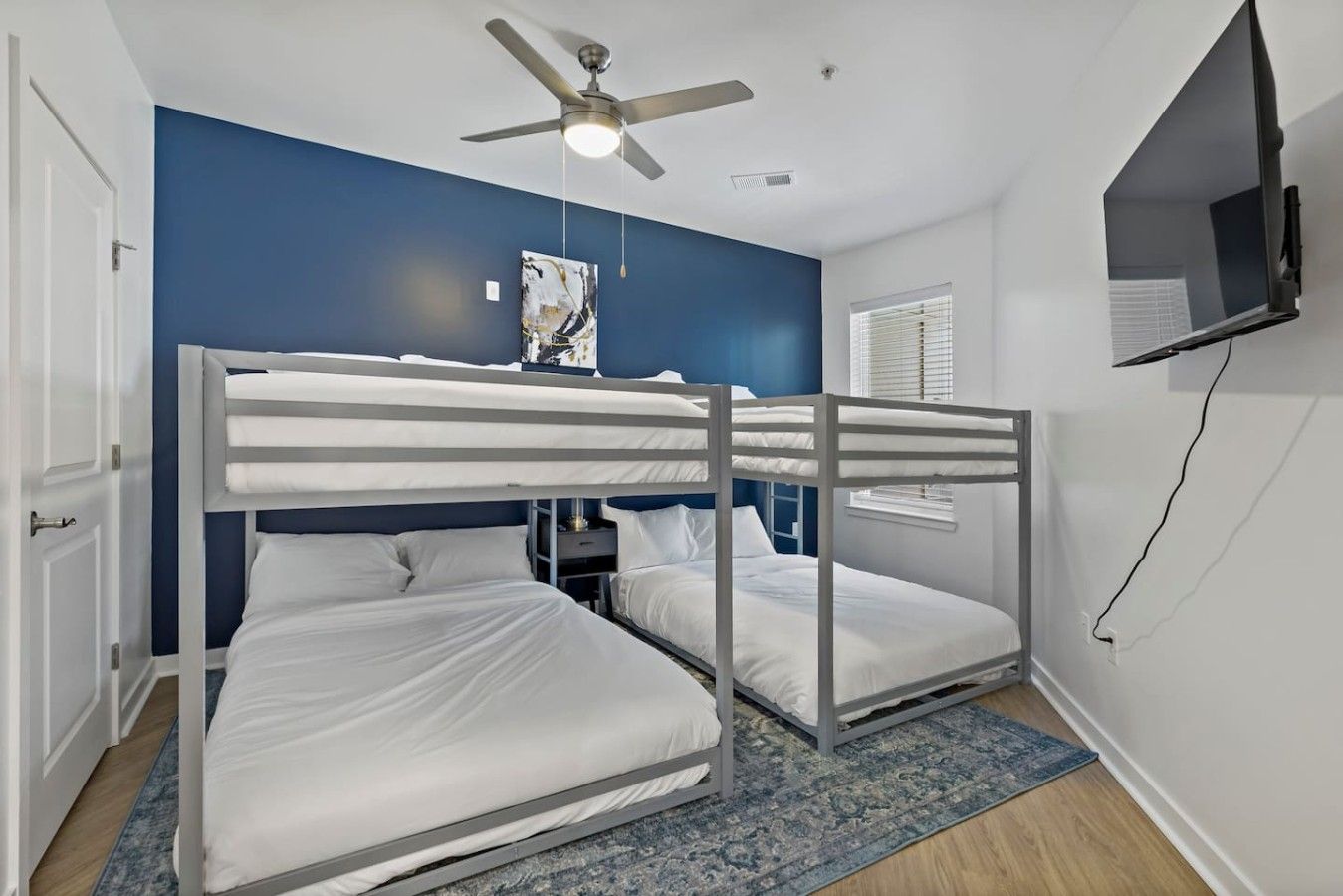 A room with bunk beds, a ceiling fan, a painting, and a television on the wall.