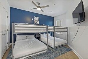 Una habitación con literas, ventilador de techo, un cuadro y televisor en la pared.