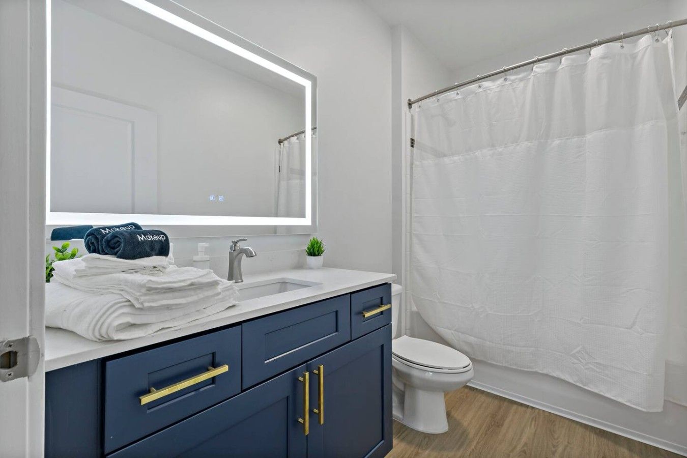 A modern bathroom with a white sink, dark blue cabinets, a white toilet, and a shower curtain.