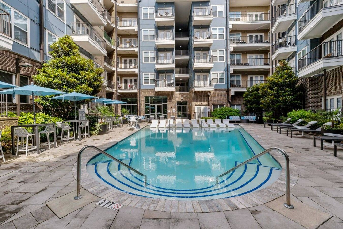 A swimming pool with lounge chairs and umbrellas, surrounded by multi-story residential buildings.