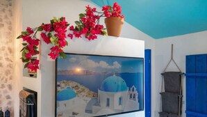 A room with a large framed painting of a coastal scene, a potted plant with red flowers, a blue door, and a towel rack.