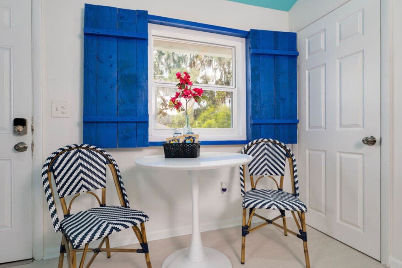 A room with two chairs, a small table, and a window with blue shutters.