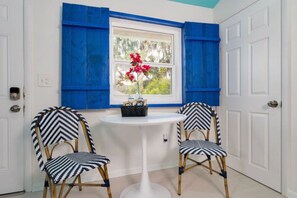 Una habitación con dos sillas, una mesita y un ventanal con contraventanas azules.