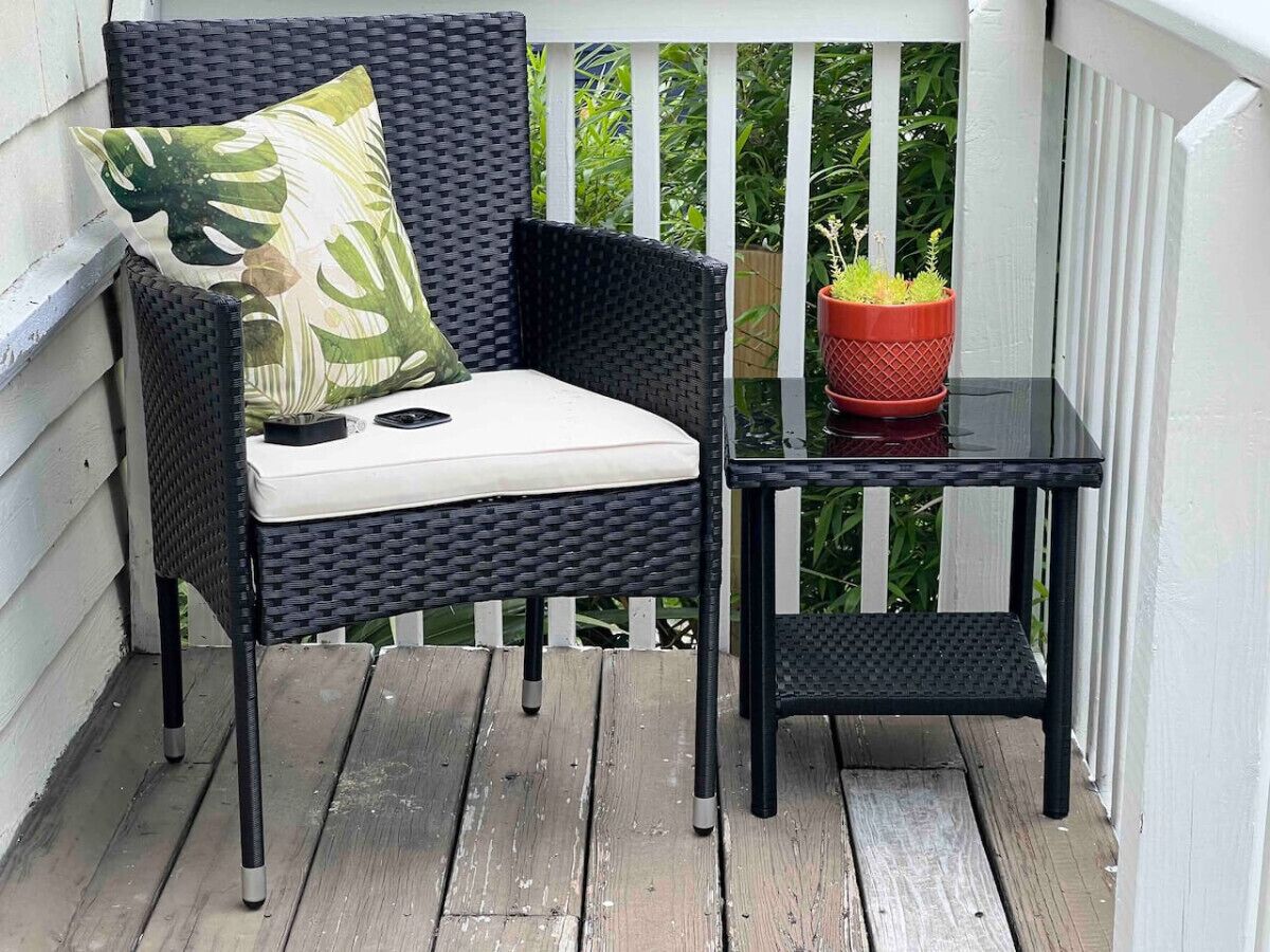 Een rieten stoel met een kussen en een klein tafeltje met een plant in een pot op een houten terras.