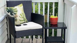 A wicker chair with a cushion and a small table with a potted plant on a wooden deck.