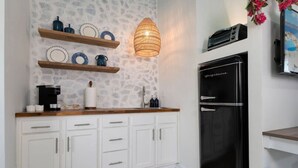 A kitchen with white cabinets, a black refrigerator, wooden shelves with dishes, and a hanging light fixture.